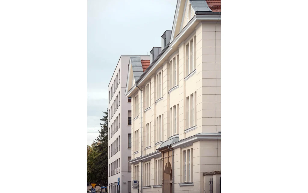 Dziedziniec kompleksu ze stalowym szybem windowym i balkonami przy zrewitalizowanej Starej Szwalni po lewej oraz nowym budynkiem z żółtymi balkonami po prawej.