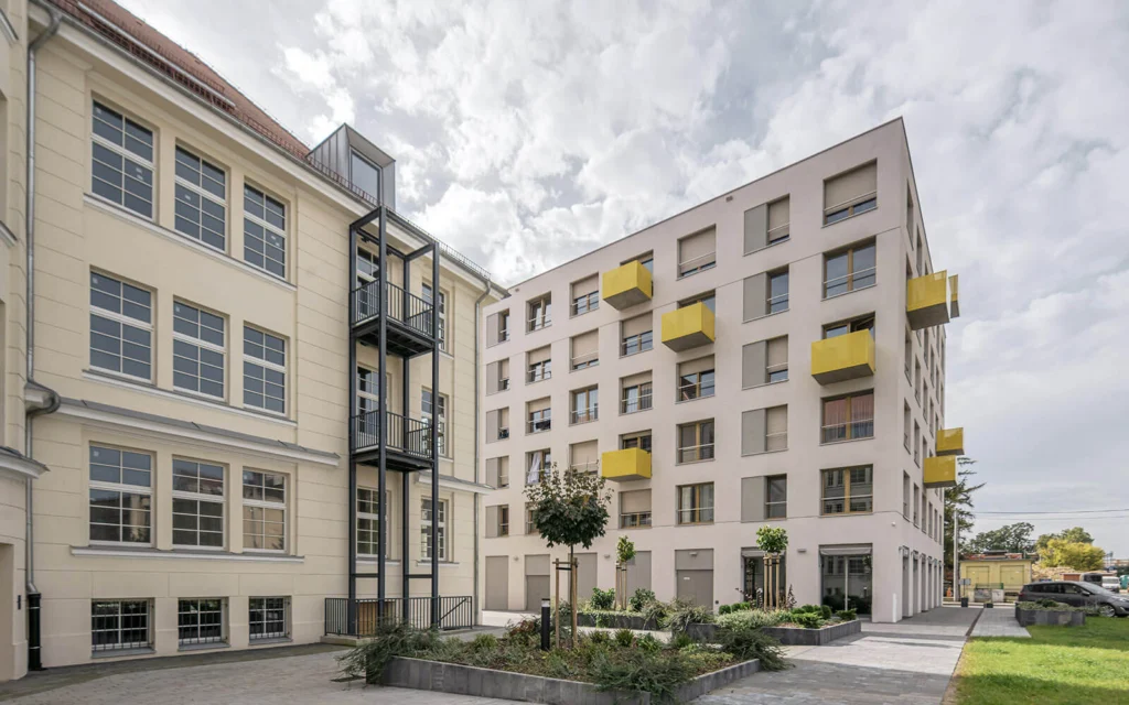 Zbliżenie na żółty, perforowany metalowy balkon wysunięty z jasnej elewacji nowego budynku.