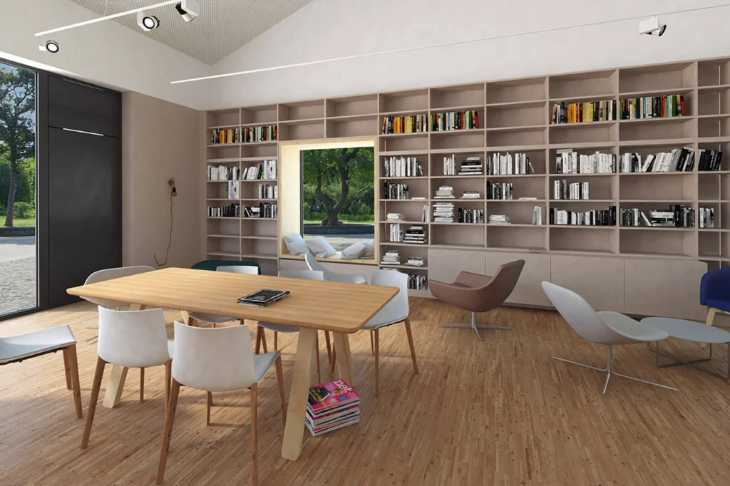 Wnętrze biblioteki w Domu Kultury z regałami pełnymi książek, wnęką z siedziskiem przy oknie i stołem do pracy pośród foteli.