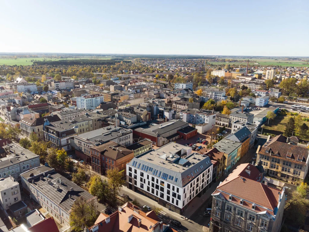 Widok z lotu ptaka na Leszno — nowy budynek mieszkalny z ciemnym dachem i białą elewacją wpisany pośród historycznej zabudowy śródmieścia.